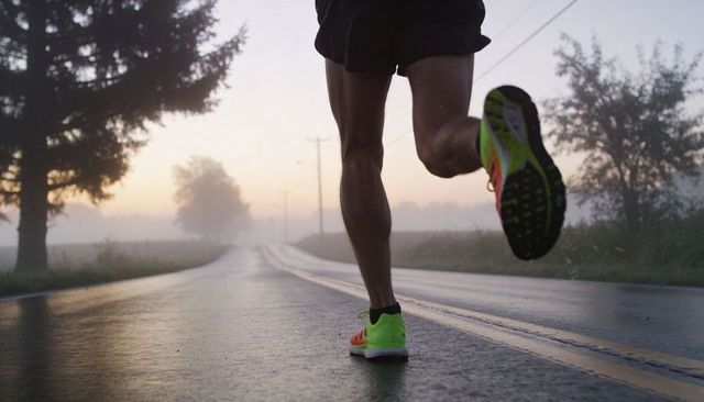Male runner sprinting on wet rural road at sunrise with neon green shoes
