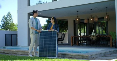 Couple holding solar panel at poolside installing residential solar for modern patio home