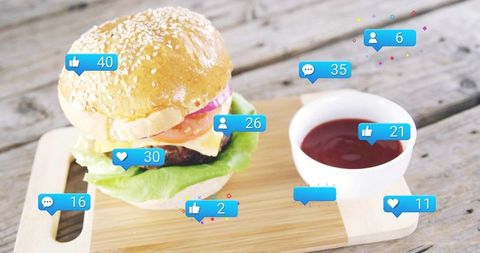 Sesame seed burger with ketchup and social media engagement icons on rustic wooden board