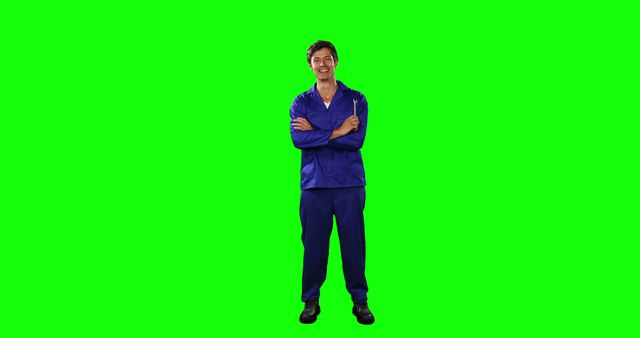 Mechanic standing with arms crossed and smiling wearing blue uniform. Perfect for advertisements, promotional materials, training videos, and tutorials related to automotive services, manufacturing, and industrial work. Green screen allows easy background replacement and integration into diverse projects.