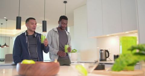 Diverse male friends enjoying green smoothies at bright modern kitchen island