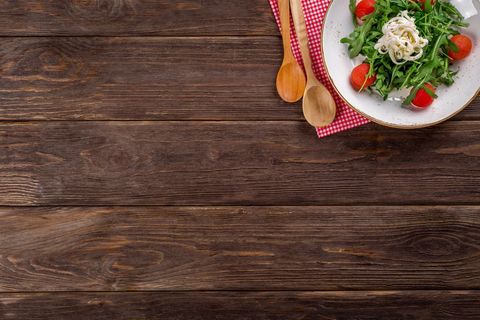 Rustic wooden table top with arugula salad, cherry tomatoes, mozzarella and wooden spoons