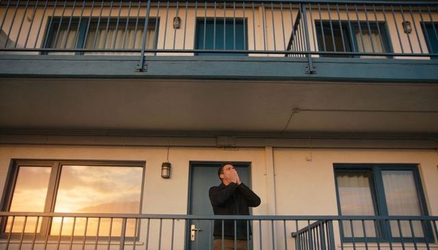 Man standing on lower balcony at sunset with blue-trim doors and metal railings