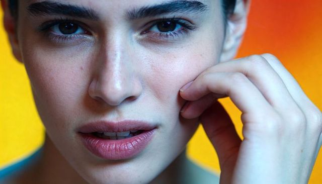 Young woman touching cheek closeup showing natural skin texture freckles warm gradient