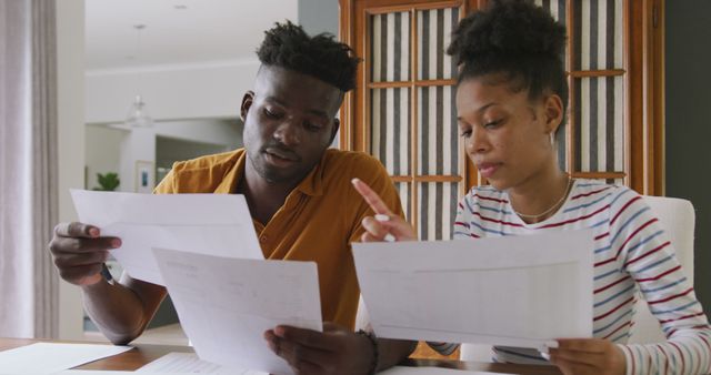 Couple focused on reviewing and analyzing financial documents together at home. Perfect for articles or advertisements related to personal finance, budget planning, financial advice, or domestic partnerships. Highlights teamwork, collaboration, and careful financial planning within relationships.