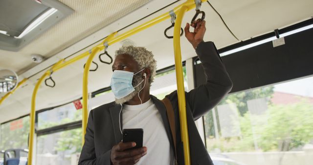 African american senior man wearing face mask using smartphone while standing in the bus. hygiene and social distancing during coronavirus covid-19 pandemic.