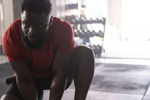 African american man preparing for workout, crouching by dumbbell rack in gym