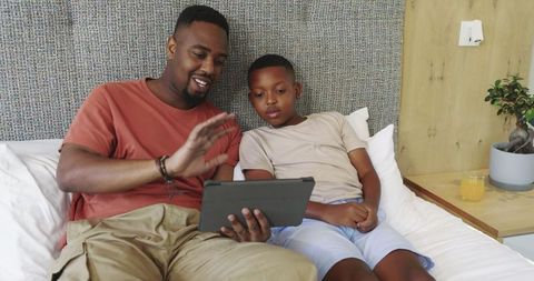 Father Sharing Moment with Son and Tablet in Cozy Bedroom