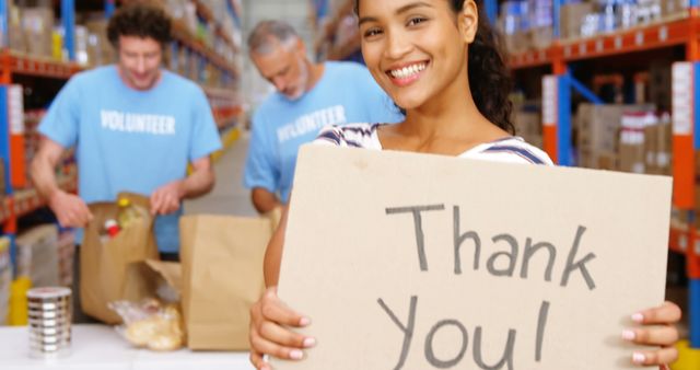 A diverse group of volunteers working at a food bank, with one holding a sign that reads 'Thank You!'. This can be used for themes related to volunteering, community service, charity work, nonprofit organizations, and food distribution events. Ideal for non-profit promotional materials, community outreach efforts, and social media posts to encourage volunteer participation and donation support.