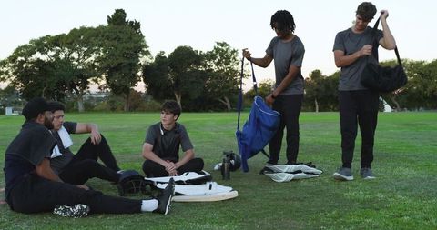 Diverse youth baseball team gathering and unpacking gear on field at dusk for practice