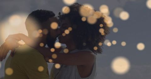 Silhouetted couple kissing at waterfront with golden bokeh lights romantic twilight scene