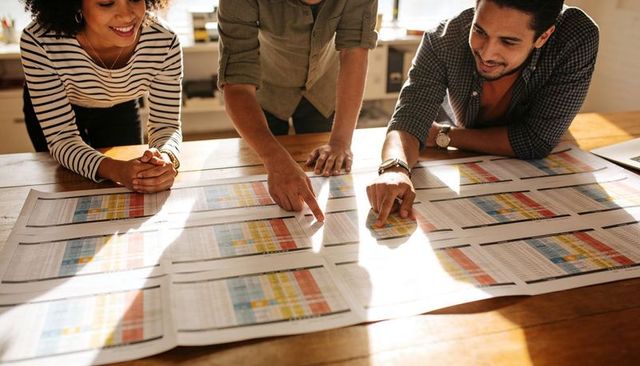 Team Collaborating Over Color-Coded Spreadsheets on Sunlit Wooden Table for Data Planning