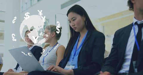 Businesswoman typing on laptop at global finance conference with currency globe overlay