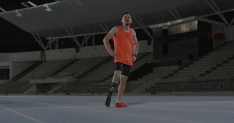 Determined Athlete with Prosthetic Blade Standing on Track under Night Lights