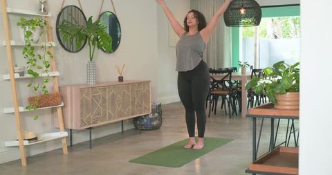 African american woman practicing yoga stretching on green mat in modern minimalist home