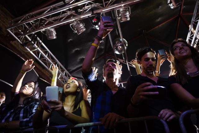 Group of people enjoying a live performance in a nightclub, capturing the moment with their smartphones. Ideal for use in articles or advertisements related to nightlife, music events, social gatherings, and entertainment venues.
