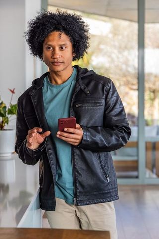 African american man holding red smartphone and gesturing in modern open-plan kitchen