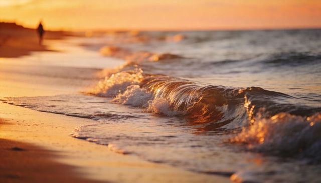 Sunlit rolling wave glowing on wet sand at golden hour with distant serene beach walker