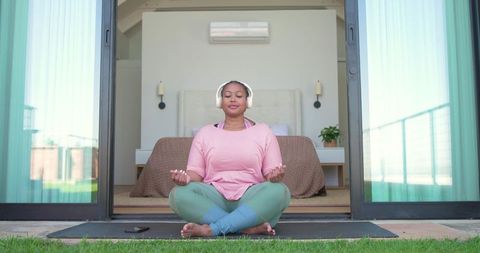 African american woman meditating on balcony wearing headphones practicing outdoor yoga mindfulness
