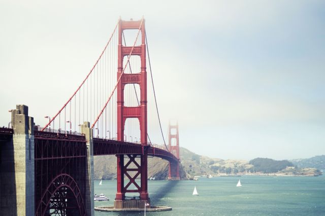 Image shows Golden Gate Bridge partially covered in fog, with several boats scattered across the bay. Ideal for travel websites, promotional materials, and blogs focusing on San Francisco, architecture, or coastal tourism. Perfect addition to articles about prominent landmarks or foggy weather conditions.