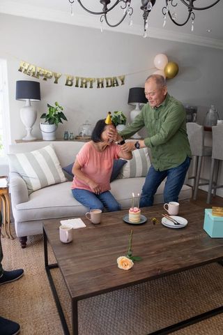 Senior asian couple surprise birthday at home, husband covering wife eyes, cake with candles