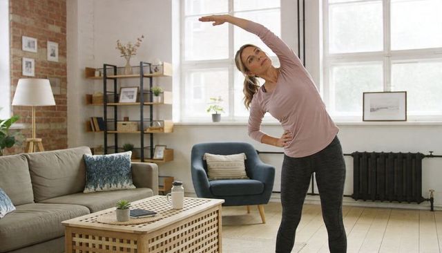 Woman doing side stretch in bright living room for home fitness and flexibility