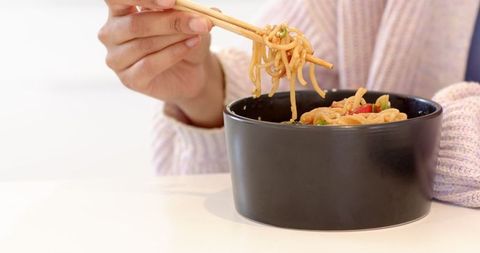 Woman Enjoying Asian Noodles with Chopsticks Indoors