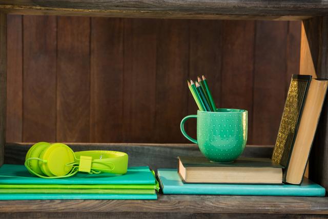 This image showcases a neatly organized bookshelf featuring green accessories such as a mug with pencils, headphones, and books. Ideal for use in articles or advertisements related to home decor, study spaces, organization tips, or lifestyle blogs.