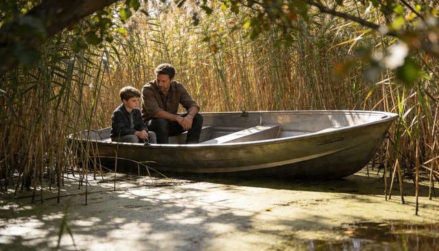 Father and son sharing quiet moment, sitting in metal rowboat among golden marsh reeds