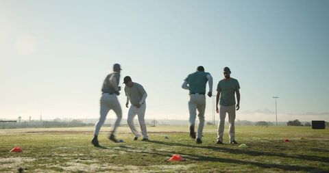 Baseball players running agility drill on grass at golden hour with cones for practice
