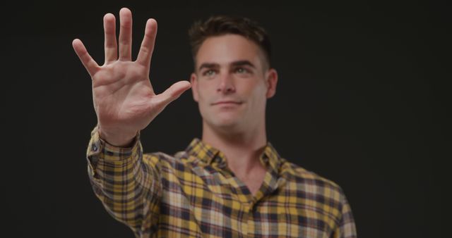 Young Man Holding Hand Up in Calm Gesture Against Dark Background - Download Free Stock Images Pikwizard.com