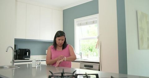 Woman in pink top adjusting smartwatch in modern kitchen morning routine