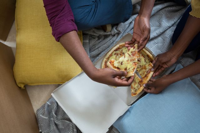 Couple sharing pizza while sitting on floor surrounded by moving boxes and blankets. Perfect for themes related to moving, new beginnings, casual dining, and home life.
