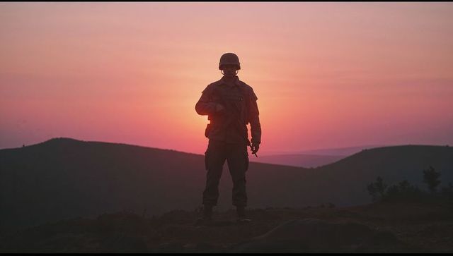 Silhouette of soldier on mountain at sunset with combat gear