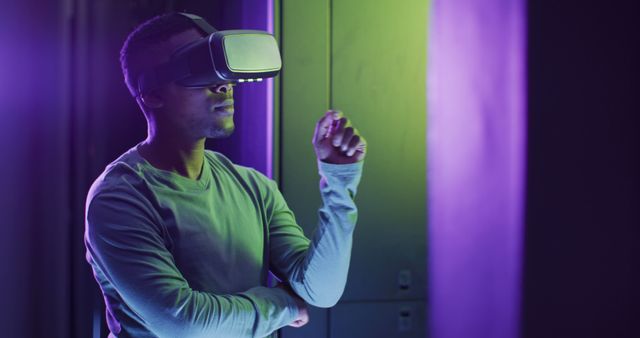 Man in neon lit room wearing a virtual reality headset, engaging in an immersive experience. Ideal for use in tech blogs, VR gaming promotions, innovation demonstrations, or futuristic themes.