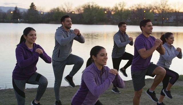 Twilight lakeside group training performing synchronized high-knee lunges for outdoor fitness