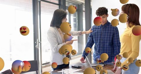 Team discussing feedback surrounded by floating emoji reactions in sunlit modern office