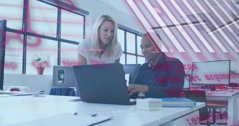 Female Mentor Guiding Colleague Over Laptop with Red Data Overlay in Bright Modern Office