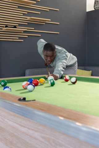 African american man concentrating while aiming cue on pool table in modern lounge