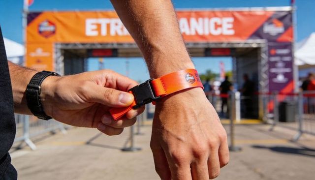 Fastening orange event wristband at festival entrance checkpoint, staff securing access