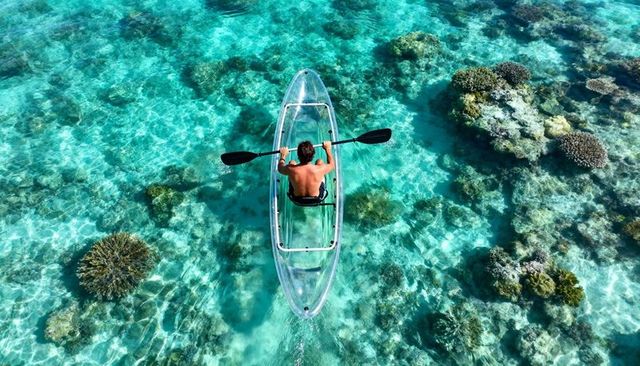 Paddling transparent kayak over turquoise coral reef top-down tropical lagoon drone view