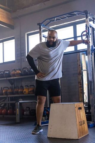 African american man resting on power rack in industrial gym during strength training