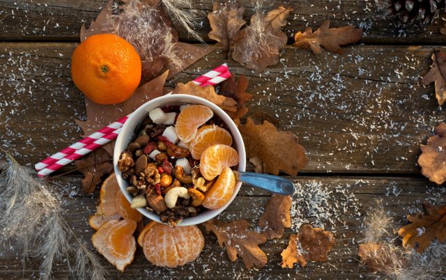 Healthy breakfast spread featuring a bowl of dry fruits and fresh orange wedges on a rustic wood table with autumn leaves. Ideal for use in health and wellness blogs, food magazines, recipe websites, or social media posts promoting nutritious meal choices and seasonal autumn themes.