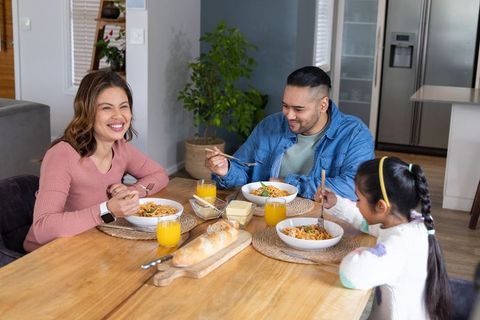 Smiling family sharing pasta dinner at home kitchen table, cozy mealtime together