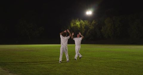 Night Cricket Players Celebrating Under Floodlights on Green Outfield During Match
