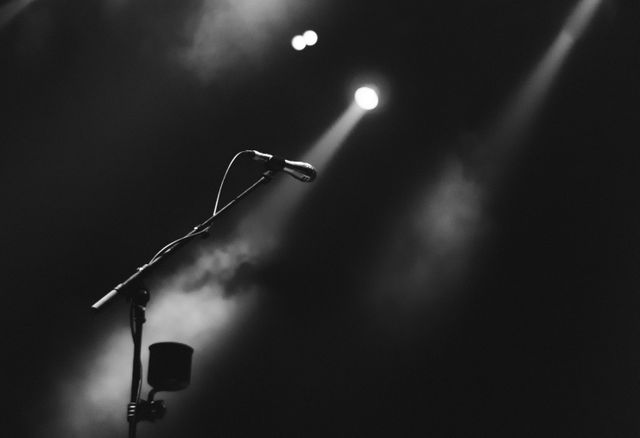 An empty microphone stand waits on stage under dramatic lighting, creating a sense of anticipation and readiness for a performance. This image is perfect for music event promotions, concert flyers, stage performance concept illustrations, or blog posts about live music anticipation and stage presence.