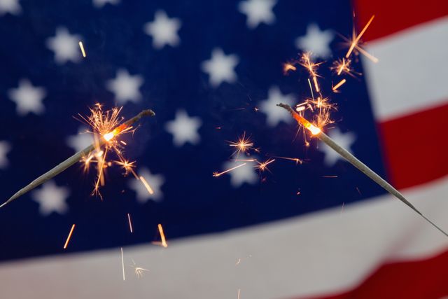This image captures the festive spirit of American national holidays like Independence Day and the Fourth of July. The close-up of sparklers burning against the backdrop of the American flag symbolizes celebration and patriotism. Ideal for use in promotional materials, social media posts, and advertisements related to national holidays, patriotic events, and celebrations.