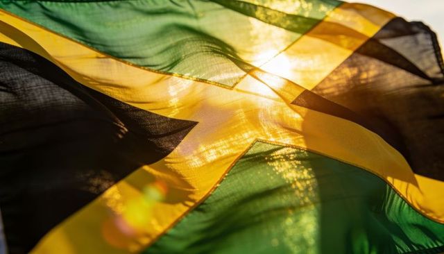 Waving jamaican flag backlit by sunlight with gold diagonal cross and translucent texture