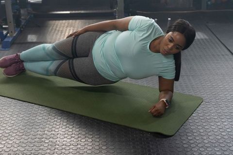 African american woman performing side plank on mat in gym wearing smartwatch