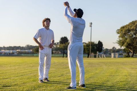 Two cricketers practicing high catch on suburban cricket field at golden hour